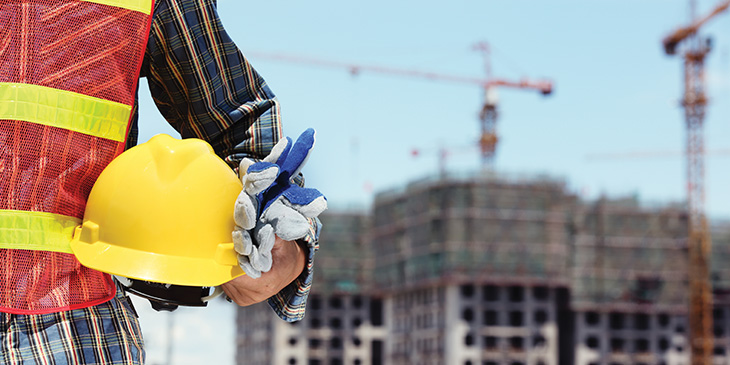 a construction worker holding a yellow helmet in front of a construction site
